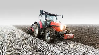 Snow falling in field with red tractor.