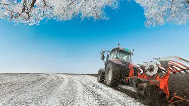 Tractor plowing field during snow in winter.